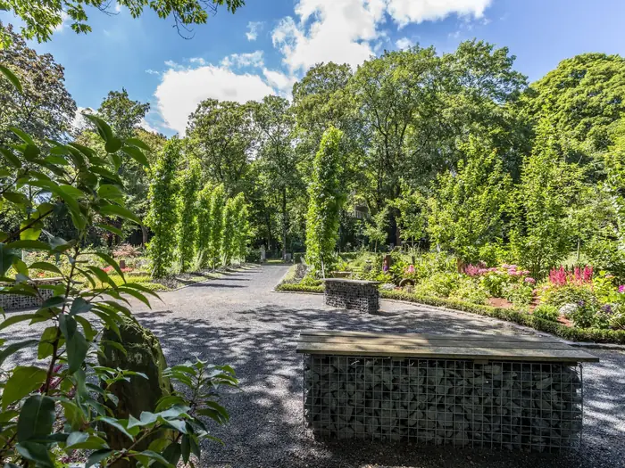 Gepflegte Gartenanlage auf dem Friedhof mit Hecken, Kiesweg und Sitzgelegenheit