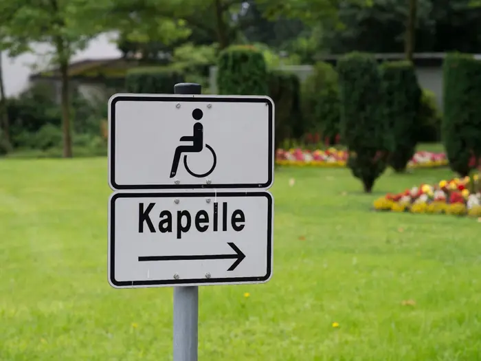 Hinweisschild zur Kapelle mit Rollstuhlsymbol auf einem Friedhof