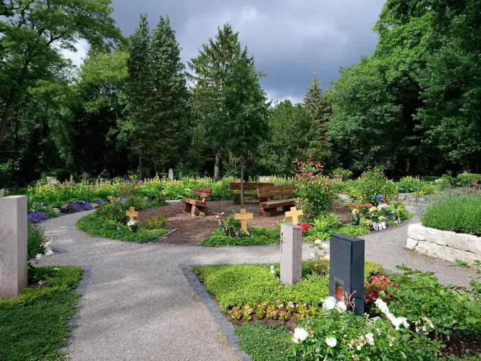 Parkähnliche Friedhofsanlage mit geschwungenen Wegen, bepflanzten Gräbern und alten Bäumen