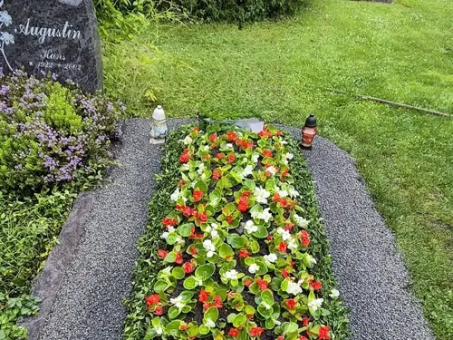 Ein mit Steinen eingefasstes Blumenbeet mit farbenprächtigen Blüten auf einem Friedhof